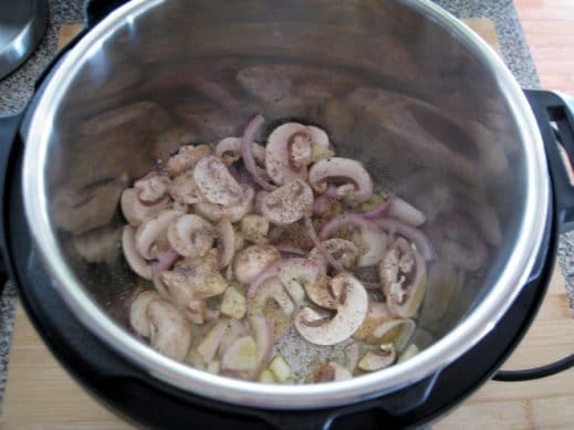 looking down into InstantPot insert filled with uncooked sliced mushrooms and roughly chopped garlic and shallots