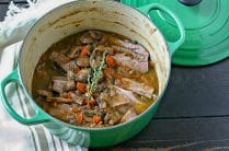 green enamel cast-iron pot with cooked passover brisket and vegetables topped with fresh thyme