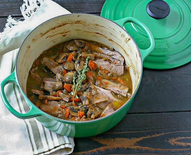 green enamel cast-iron pot with cooked passover brisket and vegetables topped with fresh thyme