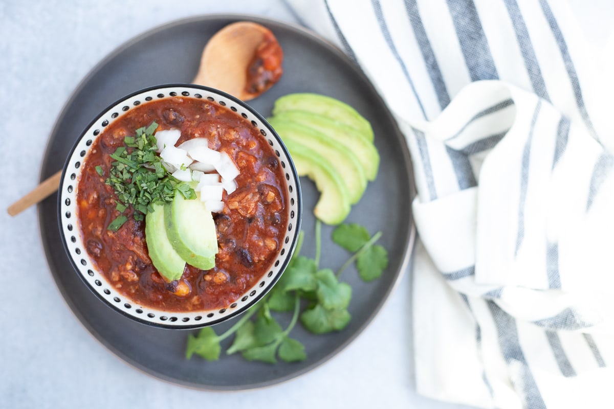 bowl of chili topped with chopped cilantro, onion and avocado