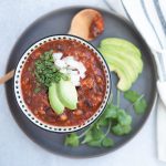 bowl of chili with toppings and wood spoon on a grey platter