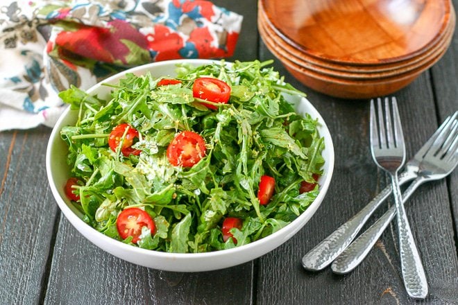 bowl of arugula salad with cherry tomatoes and wood bowls for serving