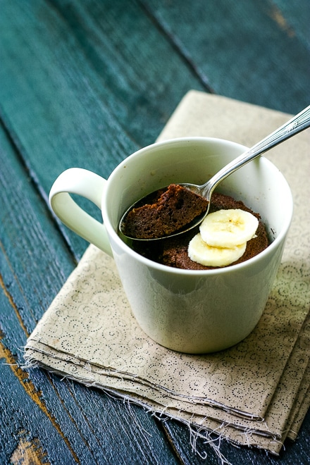 chocolate mug cake in a beige mug with a spoon and sliced banana