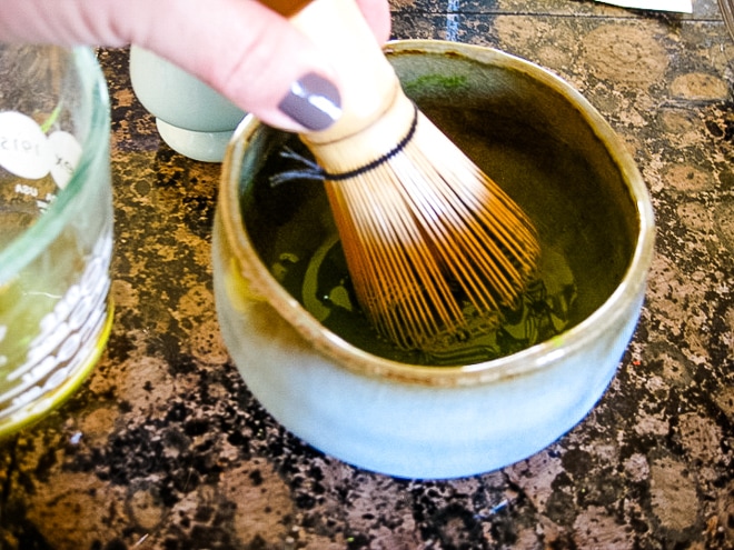 using a bamboo whisk to make a smooth matcha paste in a bowl