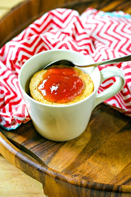 peanut butter mug cake topped with strawberry jelly with a silver spoon on a tray