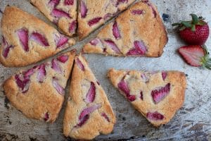 gluten free scones made with fresh strawberries on a baking sheet with a sliced fresh strawberry