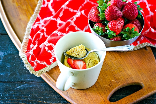 vanilla mug cake in a beige mug topped with sliced strawberries