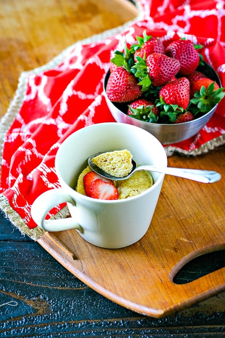 vanilla mug cake in a small mug with a silver spoon and bowl of strawberries