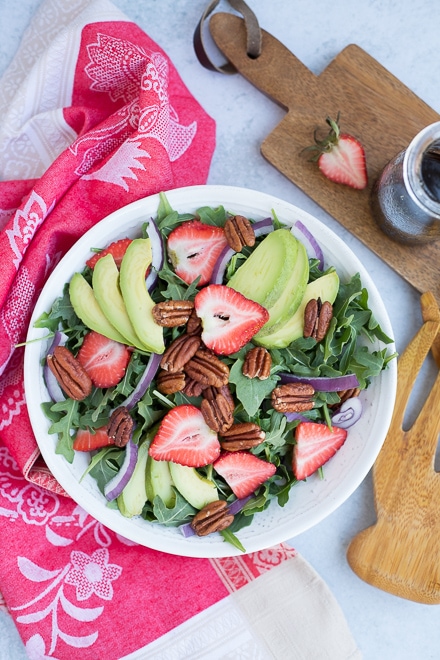 overhead view of strawberry salad with avocado, pecans and red onion on a bed of arugula