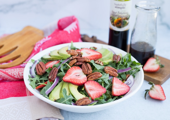 strawberry salad in a white serving bowl with balsamic dressing in a glass jar