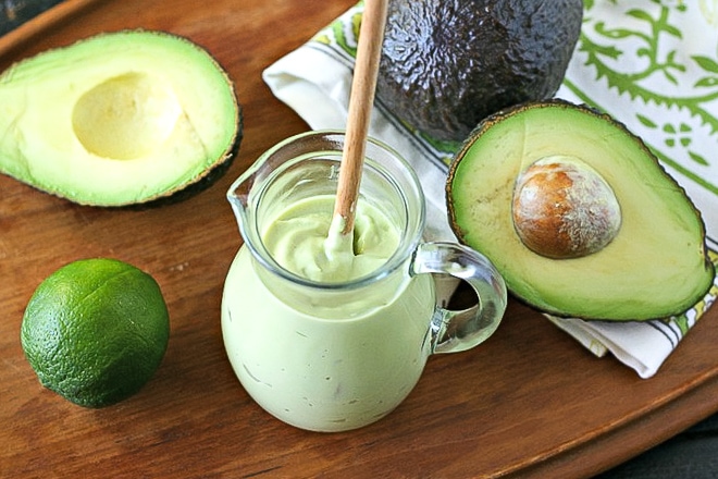 Avocado Crema recipe in a glass jar with cut avocadoes and lime