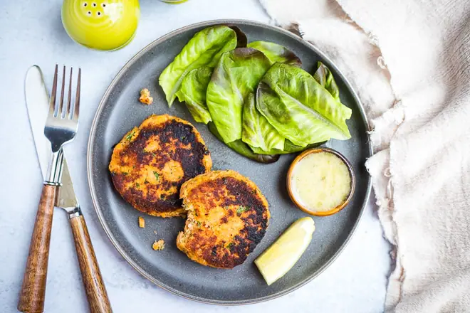 overhead shot of cooked salmon cakes on a plate with lettuce, dipping sauce and lemon