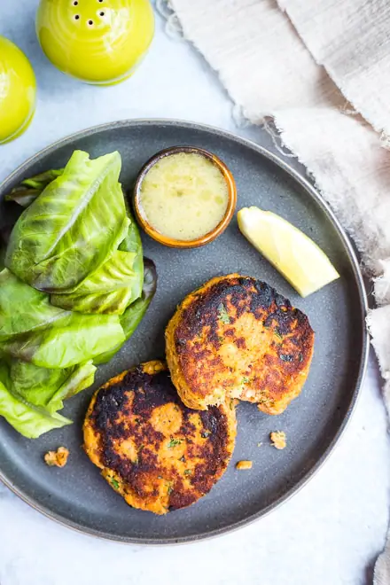 grey plate with cooked salmon cakes, salad, lemon wedge and dipping sauce