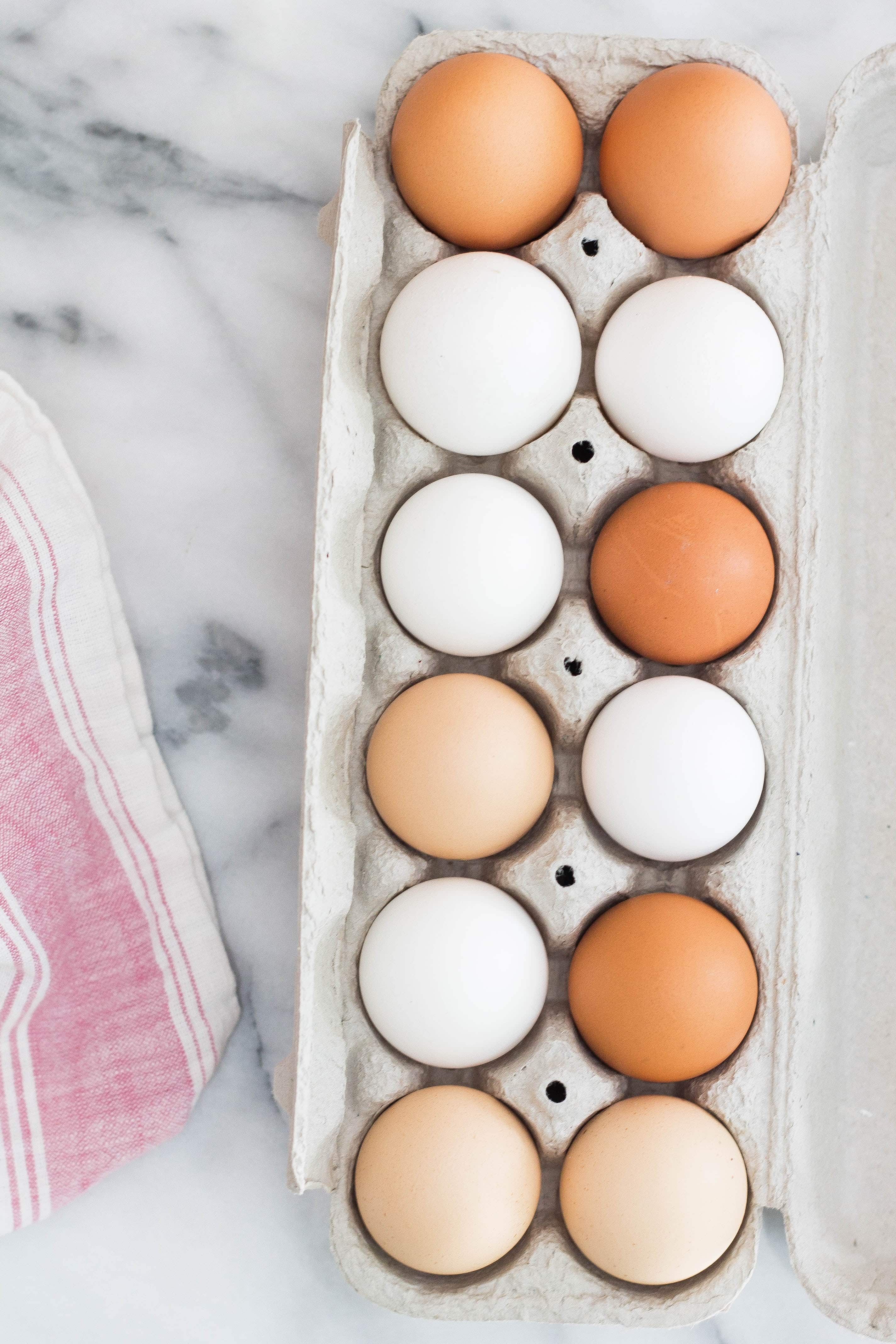 white and brown eggs in a container on a marble counter 