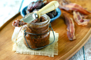 jar of homemade bacon jam in front of cooked bacon and medjool dates