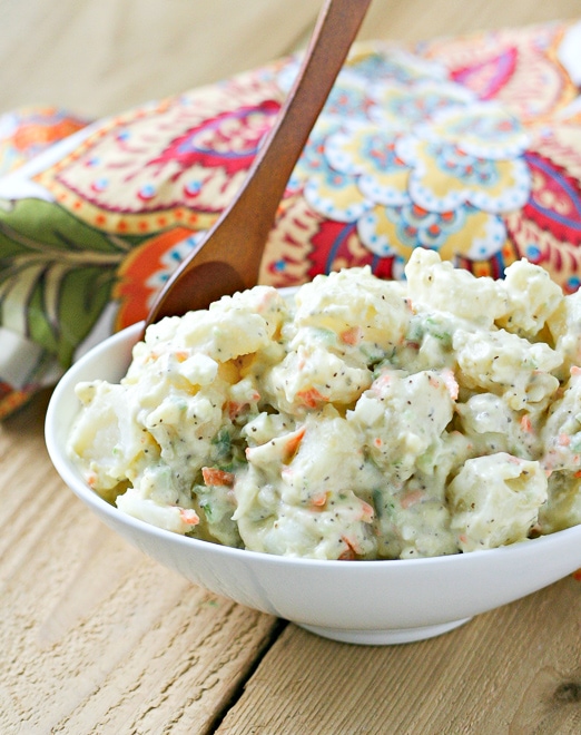 close up of classic potato salad in a white serving bowl with a brown wood spoon