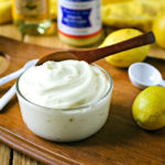 close up of homemade mayonnaise in front of lemons and dijon mustard