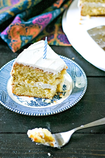 slice of gluten free vanilla cake frosted with vanilla icing on a blue plate with a fork