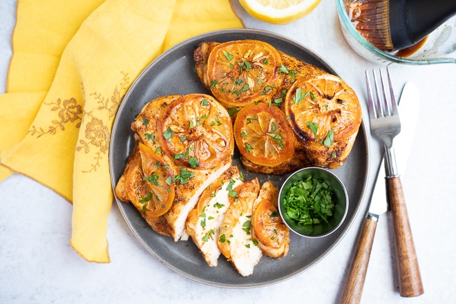baked lemon chicken sliced on a dark plate and topped with lemon and parsley