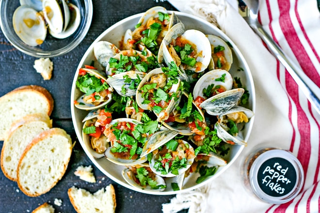 white bowl of steamed clams in tomato sauce topped with lots of parsley