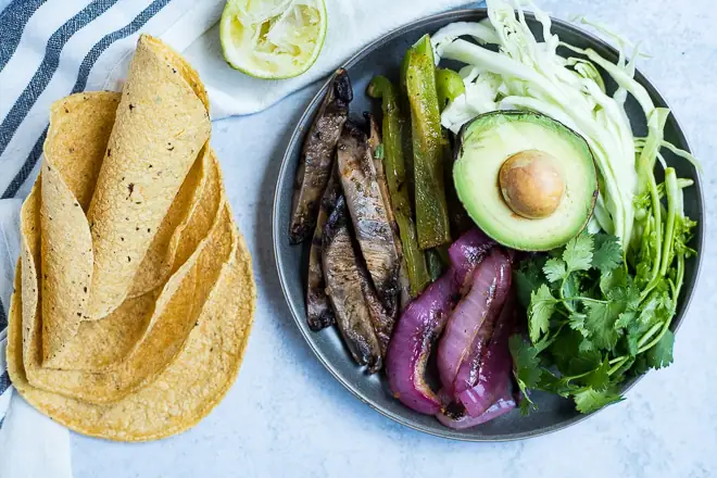 platter of cooked vegan taco filling with corn tortillas and fresh lime