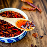 bowl of homemade chili oil with wood spoon and whole chilies