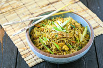 bowl of singapore rice noodles on a wood mat with chopsticks