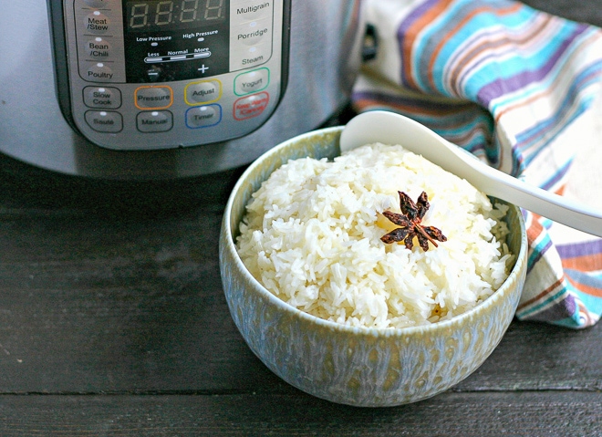 bowl of cooked instant pot rice with star anise on top in front of instant pot