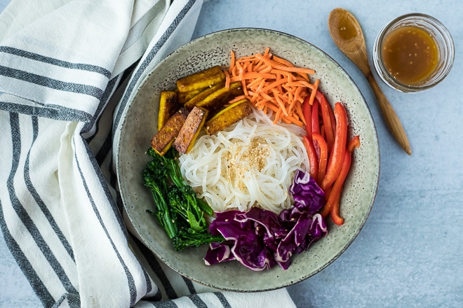 grey bowl with glass noodles and vegetables next to a striped linen
