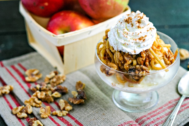 dish with ice cream and spiralized apple pie topping in front of fresh apples and walnuts