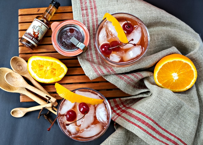 overhead of cocktails with orange slices, measuring spoons, and small bourbon bottles