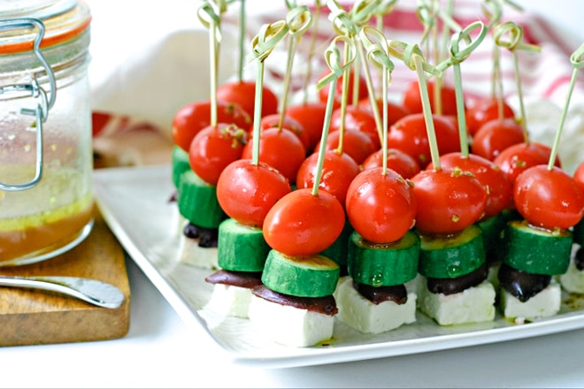 white plate with greek salad bites on a little toothpicks and bottle of dressing