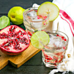 two short glasses of white sangria with pomegranate arils and lime