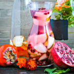 sliced pomegranate and persimmon next to a pitcher of fruit infused water