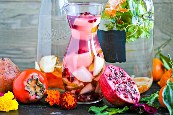 glass pitchers filled with fruit infused water with cut fruit around the bottles