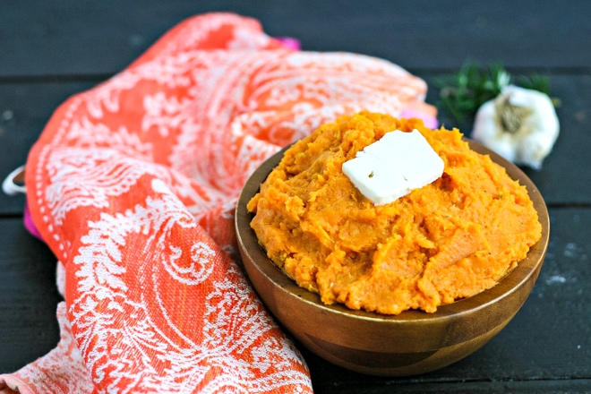 wood bowl of mashed sweet potatoes topped with butter next to an orange linen