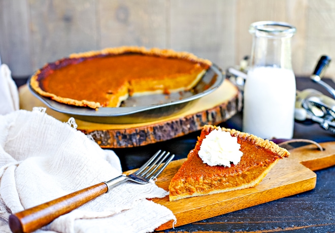 slice of paleo pumpkin pie with whipped cream on top in front of glass of milk 
