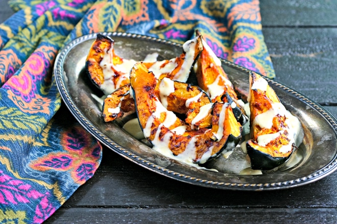 silver platter with acorn squash pieces drizzled with tahini sauce