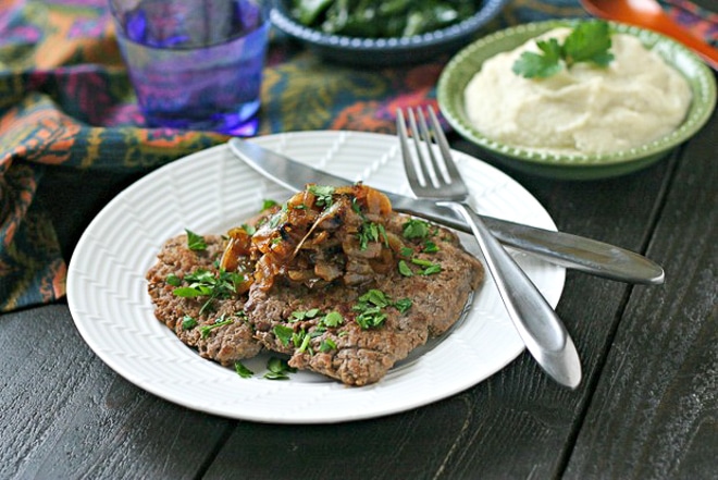 white plate with cooked cube steak topped with chopped parsley