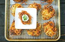 tray of potato latkes with white plate holding one latke topped with sourcream and chives