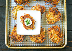 tray of potato latkes with white plate holding one latke topped with sourcream and chives