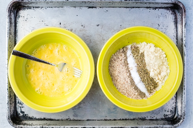 two bowls on a baking sheet with egg wash and breading mixture for gluten-free mozzarella sticks