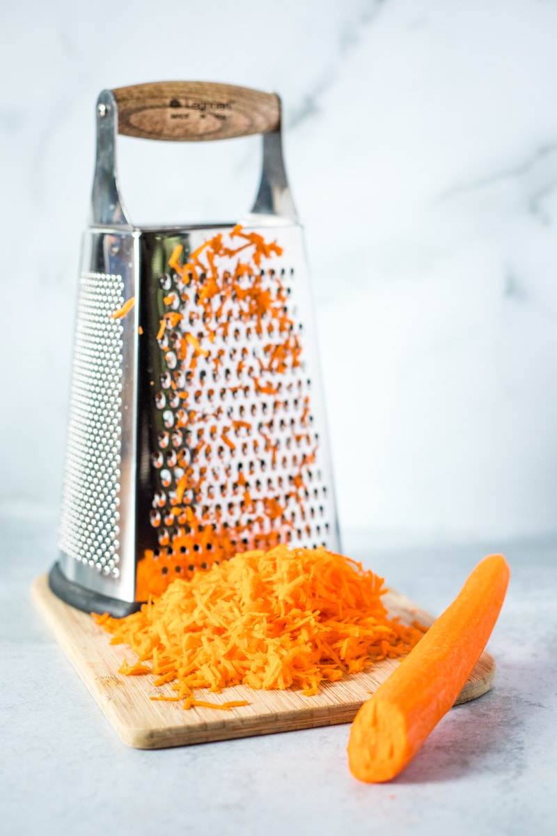 large box grater on a cutting board with grated carrots and a whole carrot