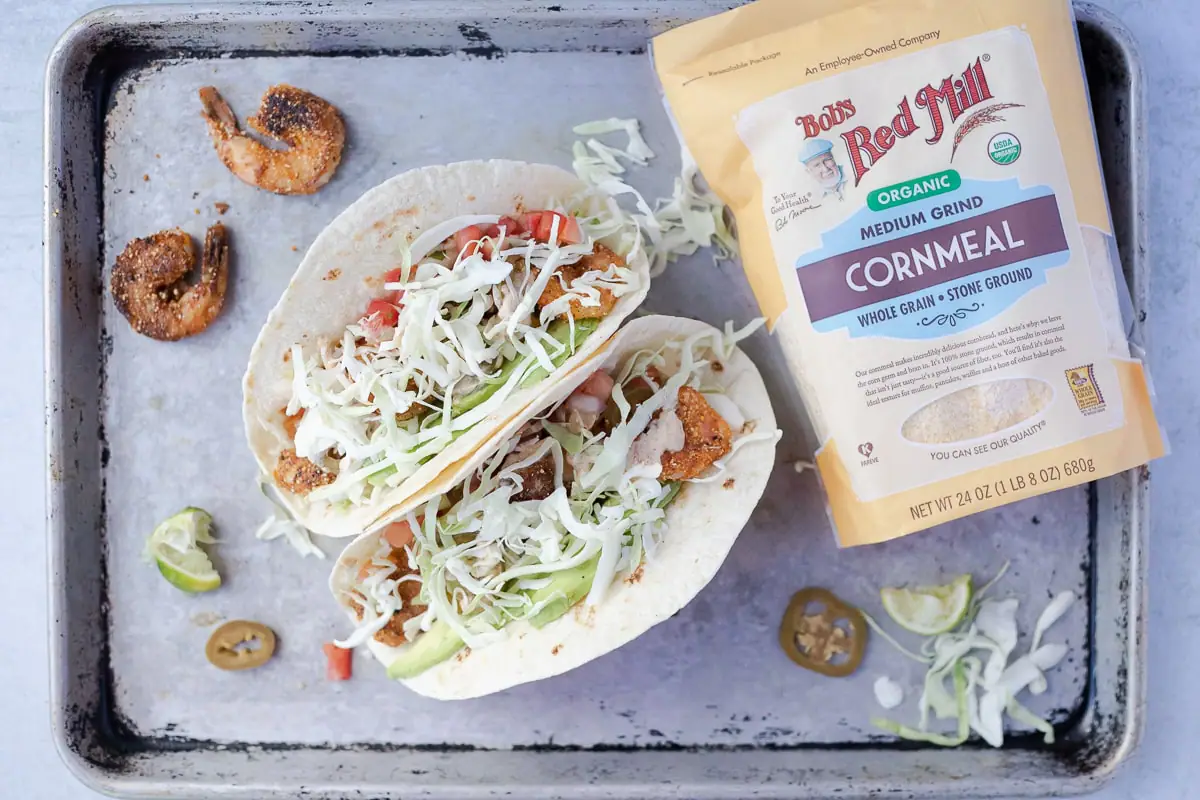 two shrimp tacos with all the toppings next to a bag of Bob's Red Mill cornmeal