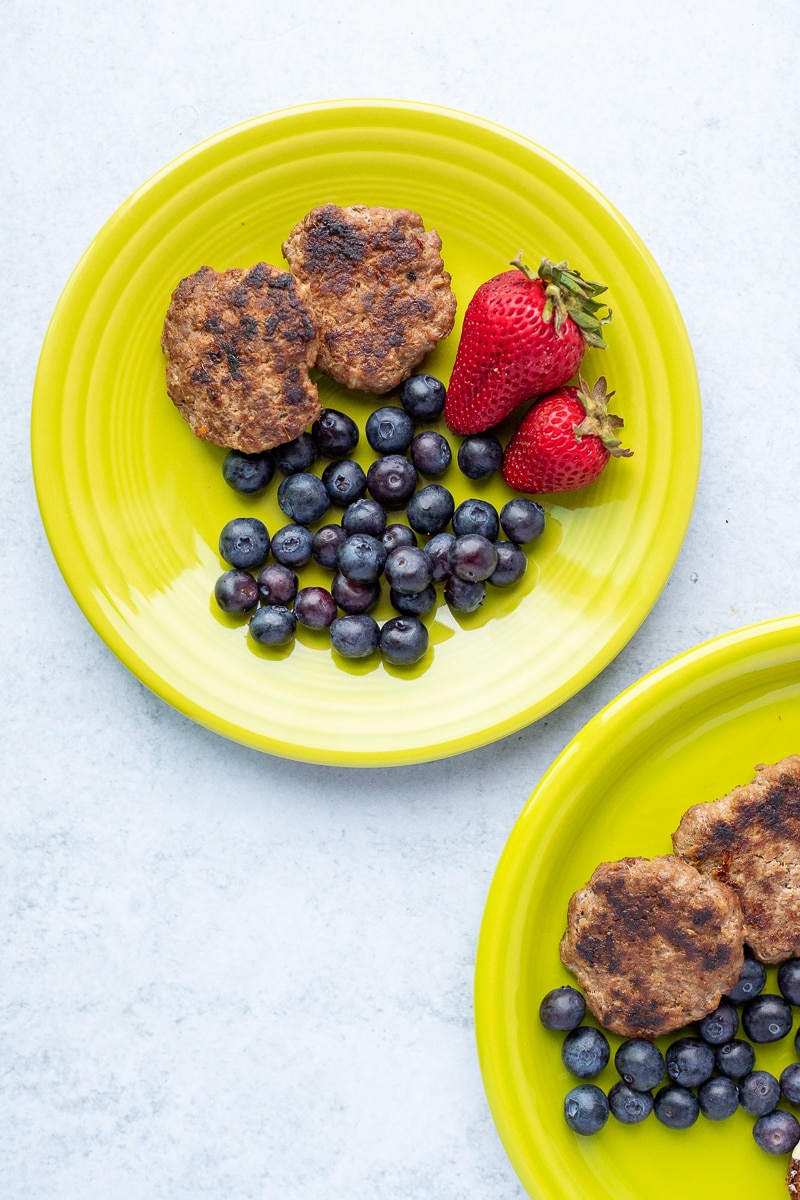 green plates with cooked breakfast sausage, blueberries and strawberries