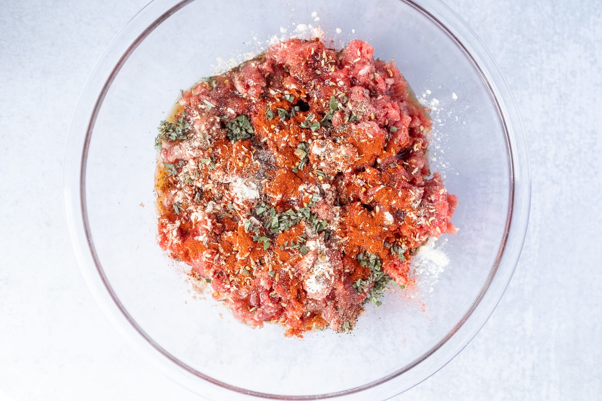 glass mixing bowl with raw ground pork and spices to make breakfast sausage