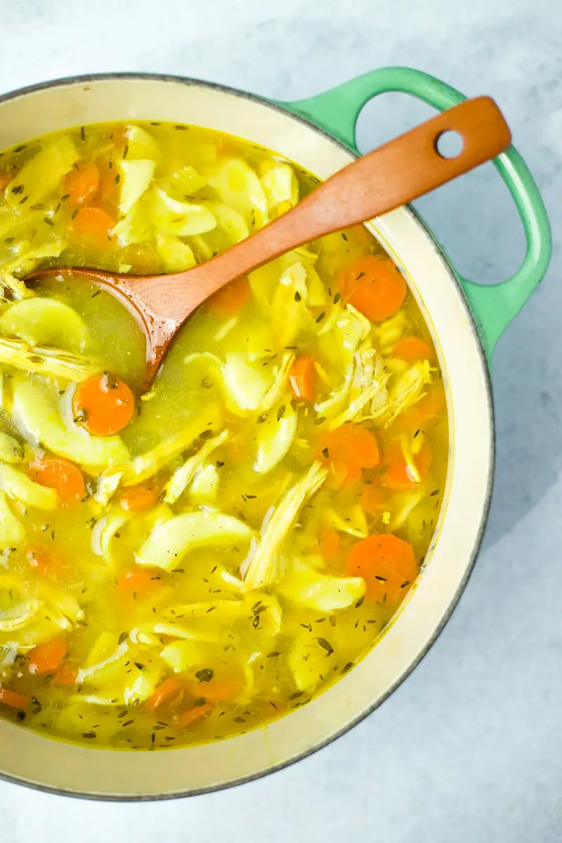 large green pot of turmeric chicken soup with brown wood serving spoon