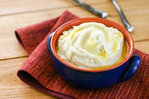 blue ceramic bowl filled with mashed cauliflower topped with melted butter