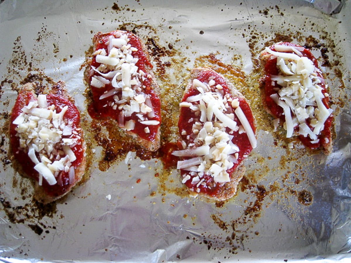 topping breaded chicken with sauce and mozzarella cheese on a baking sheet