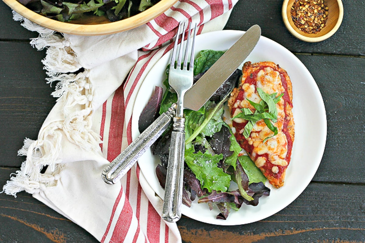 plate of gluten-free chicken parmesan with salad and knife and fork
